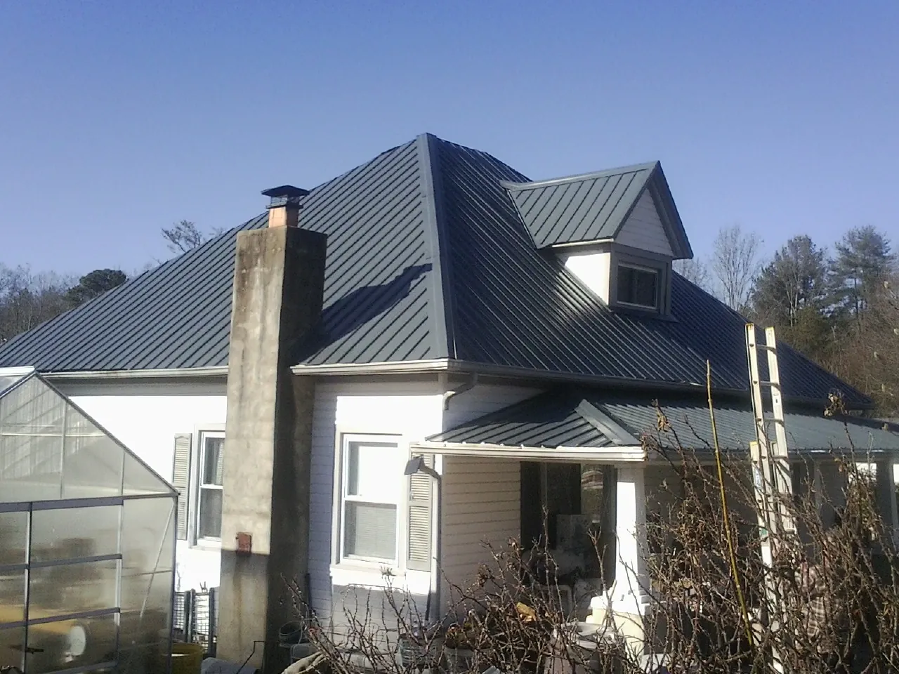 Dark blue standing seam metal roof on a white farmhouse with dormer — Slate & Tile Roof Repair by Roofing Brothers in Wisner