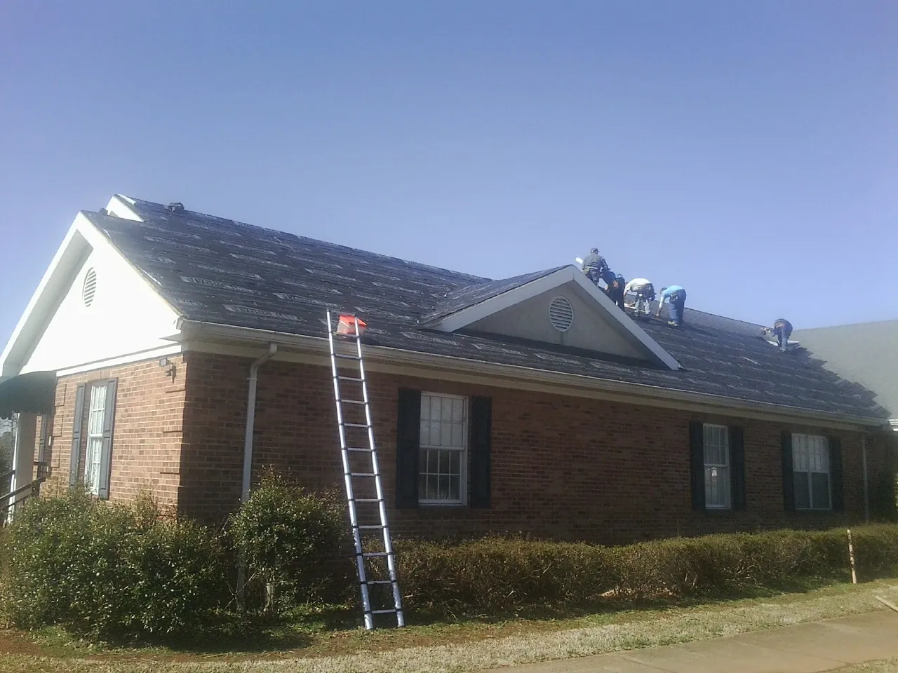 Crew tearing shingles off a brick ranch roof with a ladder set — Emergency Roof Repair work by our crew in Wisner