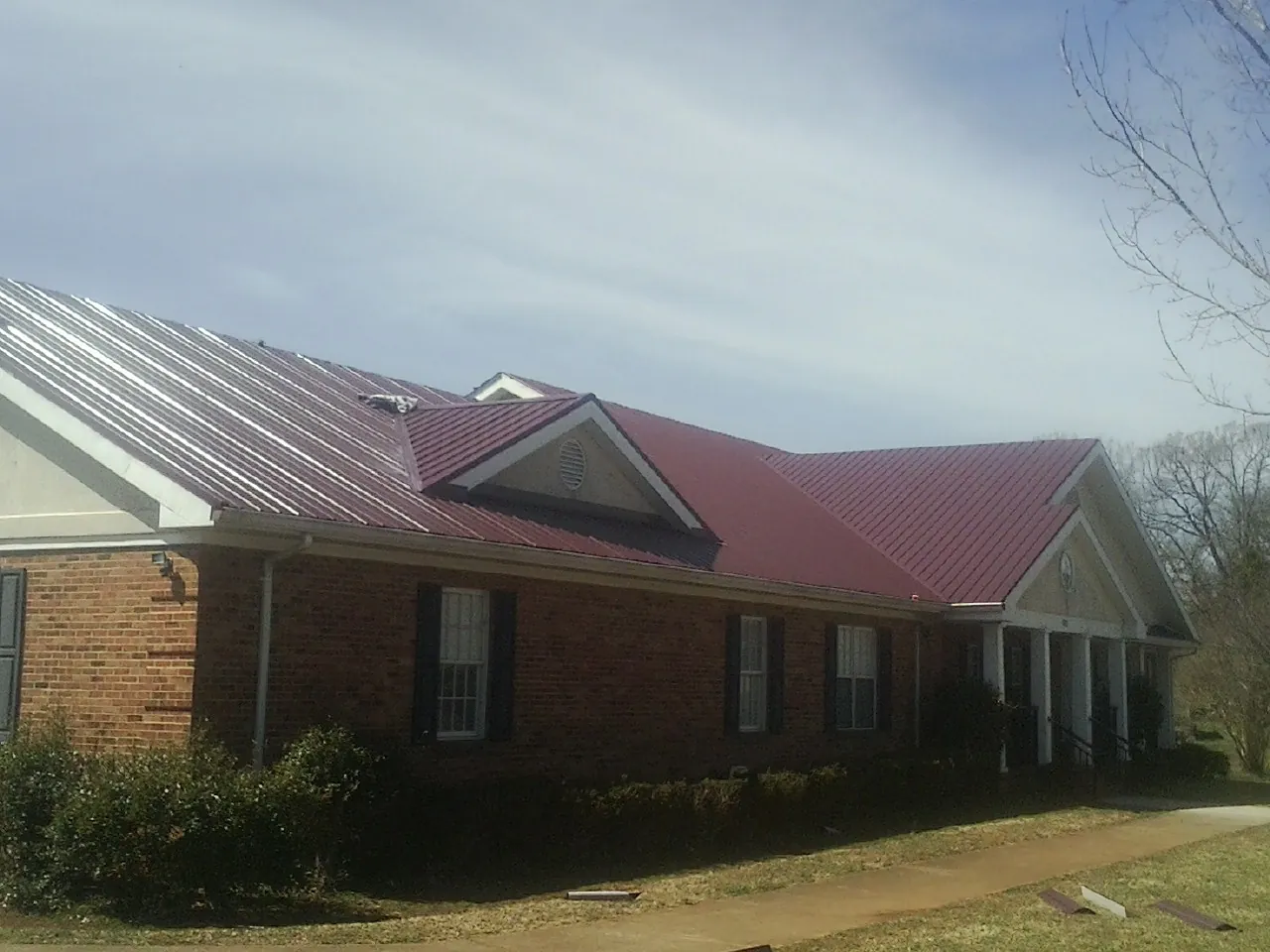 Red metal roof with gabled entries on a long brick building, from a Hail Damage Roof Repair job in Wisner