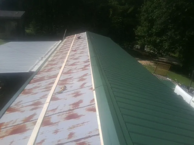Old rusted panels beside newly installed green metal roofing — Wind Damage Roof Repair by Roofing Brothers in Wisner