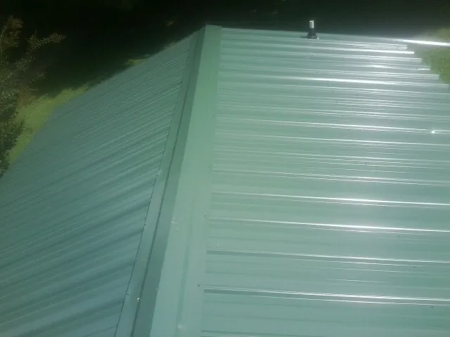 New green metal panels meeting at the ridge of a roof — Flat Roof Repair work by our crew in Wisner