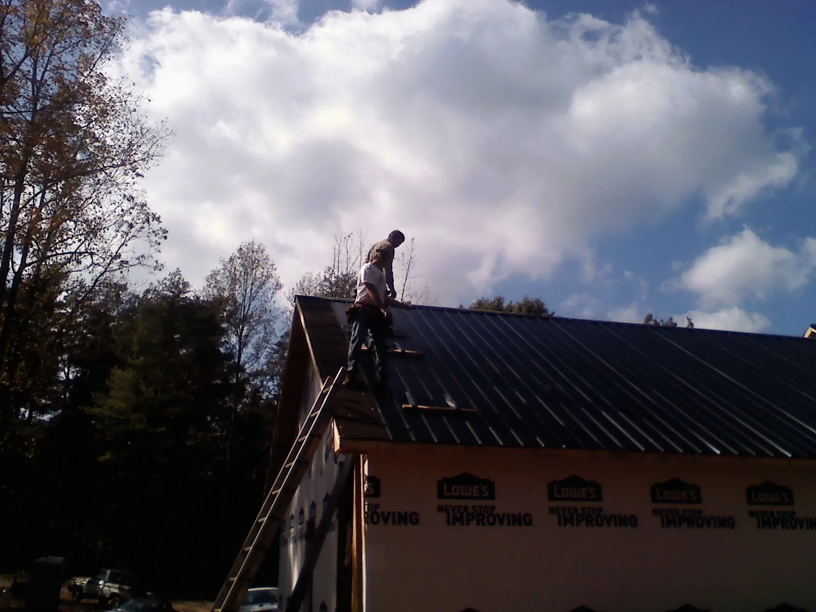 Roofer fastening dark metal panels high against a cloudy sky, from a Roof Inspection job in Wisner