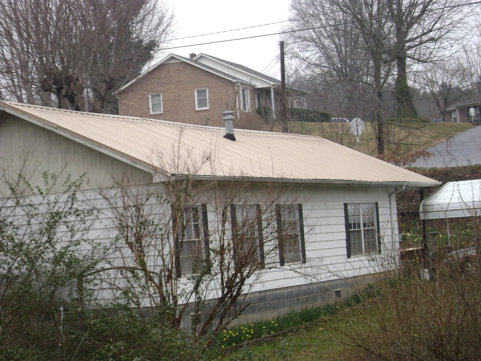 Tan metal roof on a white sided house set into a hillside — Commercial Roofing by Roofing Brothers in Wisner